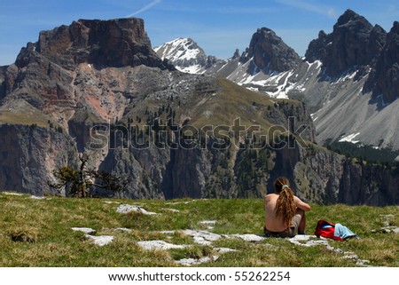 Mountain hiker resting on green meadow in front of rocky peaks