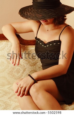 Beautiful woman with elegant black hat sitting on antique sofa