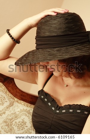 Beautiful woman with elegant black hat sitting on antique sofa