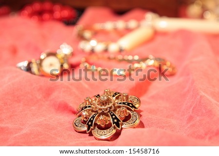 Beautiful golden brooch on red surface and more jewelry in the background