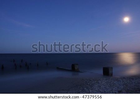 Sea at night with moon and wooden poles