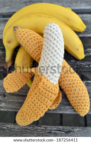 Knitted yellow bananas with real bananas on the old textured table