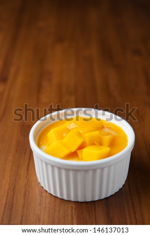 Mango dessert in a classic whiteware on wooden table, with space for text, summer recipe