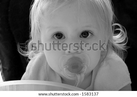 A black and white portrait of a baby with a pacifier in her mouth.