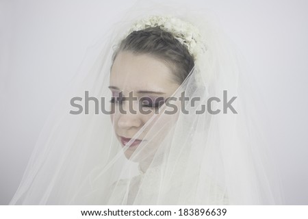 Close-up of beautiful young bride with brown hair pulled back, wearing veil and looking down.