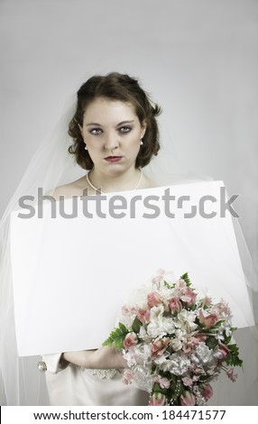 Beautiful young bride with mad expression holding blank card for copy and bouquet with pink roses