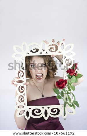 Beautiful young woman wearing strapless burgundy dress posing with white picture frame and red roses.