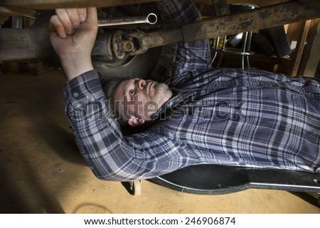 Man under car working on it with tool in his hand