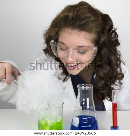 Teenage girl wearing lab coat and doing a science experiment with green and blue liquid in tubes and tongs.