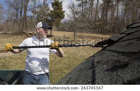 Man wearing work gloves taking shingles off a shed roof