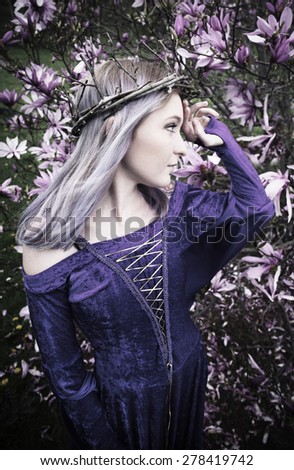 Girl wearing twig crown and purple velvet dress standing in front of magnolia tree with pink flowers