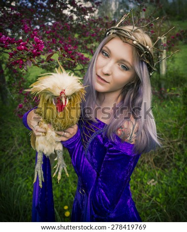 Beautiful young woman dressed as a queen wearing a velvet purple gown and twig crown and holding a chicken,