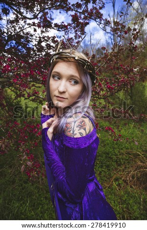 Girl wearing purple gown and twig crown standing by flowering crabapple tree
