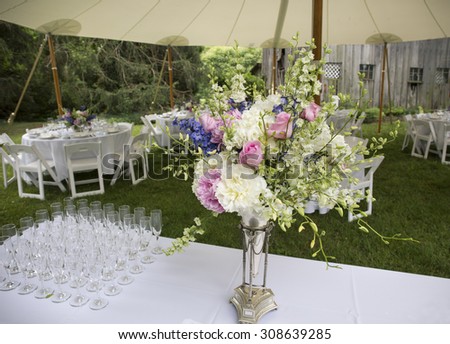 Flower arrangement and glasses and tables set up for outdoor wedding.