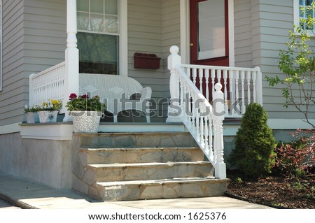 Home porch with white wicker seat, front door entrance, steps, planter with flowers