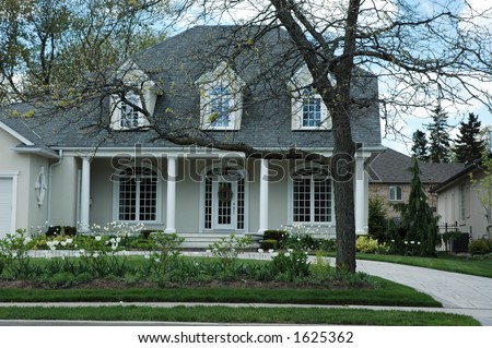 Luxury stucco house with white trim and bright green, manicured lawn / garden with white tulips and pillars by front porch
