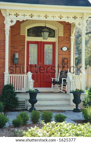 Front door entrance to victorian home with red doors, red brick, porch and two iron urns