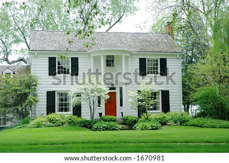 White fromal house with siding, black shutters and bright green, manicured lawn / garden