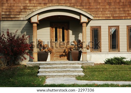 Home entrance with lots of wood trim and wooden door flanked by two planters with hydrangeas