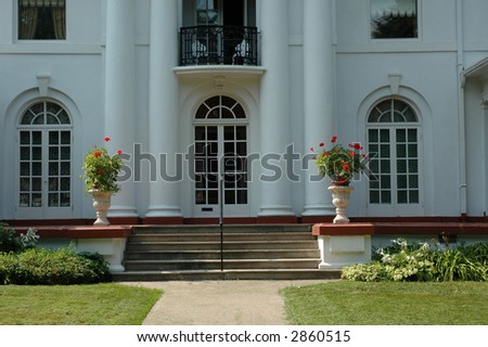 Pretty white grand luxury house / home with two urns with red geraniums