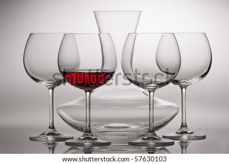 Four wine glasses and carafe. One bottle is poured of red wine.