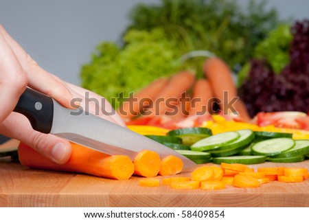 Cutting three carrot on the wooden board with vegetables on the background.
