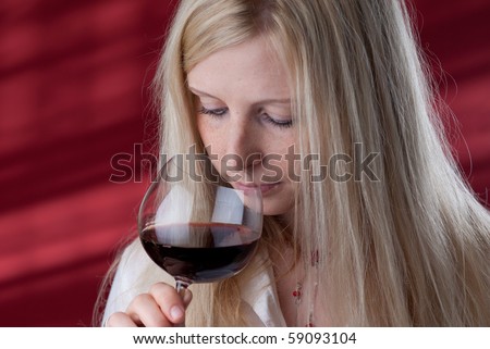 Portrait of a beautiful young woman with a glass of red wine, she is smelling.