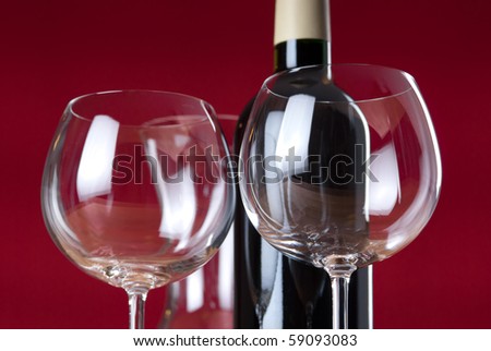 Detail of two wineglasses, red wine bottle and carafe with red background.