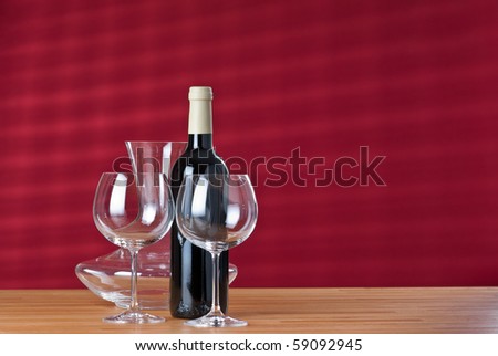 Two wineglasses, red wine bottle and carafe on wooden table with red background.