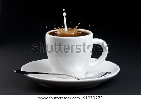 Pouring milk into coffee with splashing. White cup and black background.