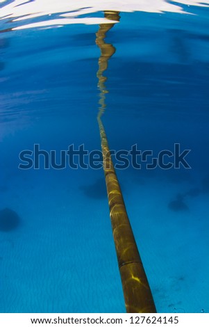Bamboo pole reflection in ocean surface over a sandy bottom