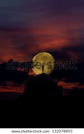 Man in silhouetteagainst a rising full moon at sunset on top of a hill on Mt. Kilimanjaro, Tanzania