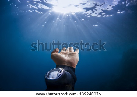 Scuba divers hand reaching out to sun light underwater on blue background in the ocean