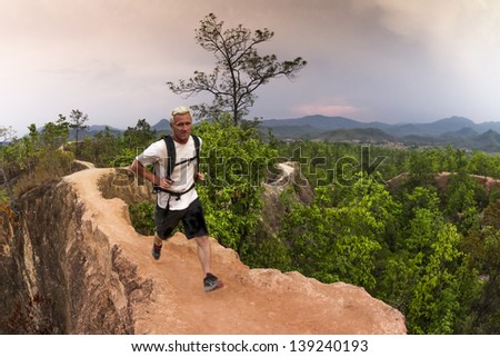 Male trail runner with white shirt and backpack running narrow path in red canyon