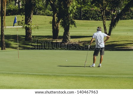 Male golfer on the green at the golf course wearing white shirt at Green Valley/St Andrews Golf course near Pattaya, Thailand