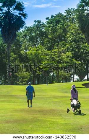 Senior golfer walking with female caddie to 5th hole at Green Valley/St. Andrews golf course near Pattaya, Thailand