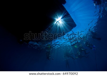 Underwater silhouette view of dive boat  and scuba divers on the surface with rays of sunlight streaming through in Koh Tao, Thailand.