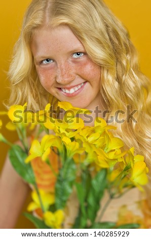 Beautiful blond girl with freckles holding a bouquet of flowers on a yellow background