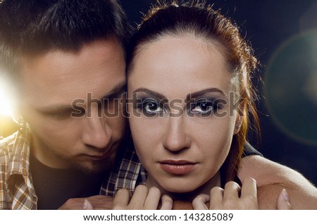 Couple of lovers. The guy holding the girl\'s neck, hugging her tightly, looking at her. The girl with two hands holding a hand guy and looking at the camera. On a black background
