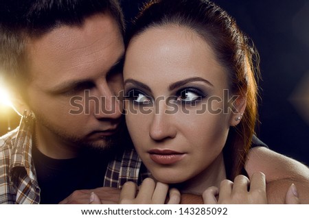 Couple of lovers. The guy holding the girl\'s neck, hugging her tightly, looking at her. The girl with two hands holding a hand guy and looks away. On a black background
