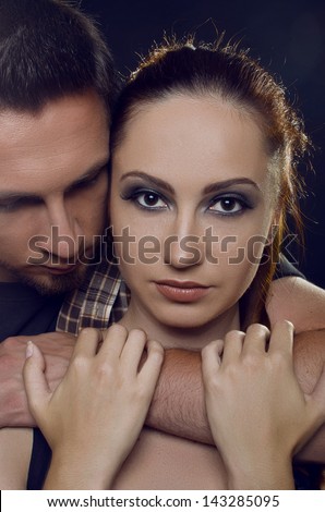Couple of lovers. The guy holding the girl's neck, hugging her tightly, looking at her. The girl with two hands holding a hand guy and looking at the camera. On a black background