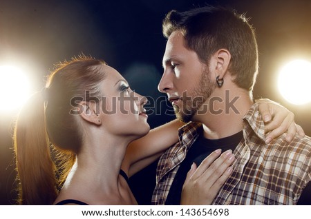 Beautiful young couple in love. The girl embraces the guy\'s neck and they look into each other\'s eyes on a black background