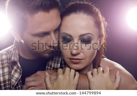 A pair of lovers. The guy holding the girl\'s neck, hugging her tightly, looking at her. Girl with two hands holding a hand guy and looks down. On a black background