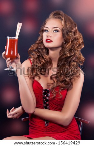 Beautiful red-haired girl in a red cocktail dress holding a cocktail with tomato juice