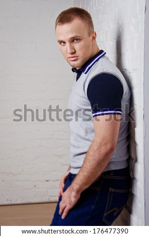 Cute guy in jeans and a t-shirt leaning against the white brick wall