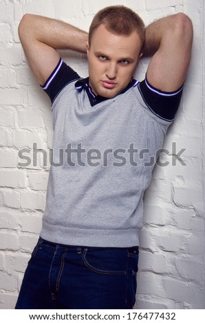 Cute guy in jeans and a t-shirt leaning against the white brick wall