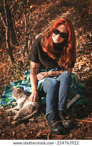 The woman went out for a walk in the park with a cat. Together they sit on the rug and bask in the sun