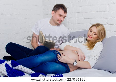 Prospective parents lie on the couch and read a book. Pregnant woman with her husband