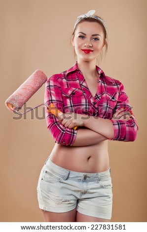Beautiful woman builder in the style of pin-up holding pink roller for painting walls