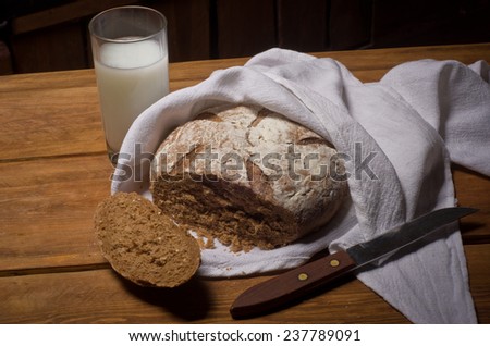 Rosy loaf of bread wrapped in white linen towel lying on a wooden table